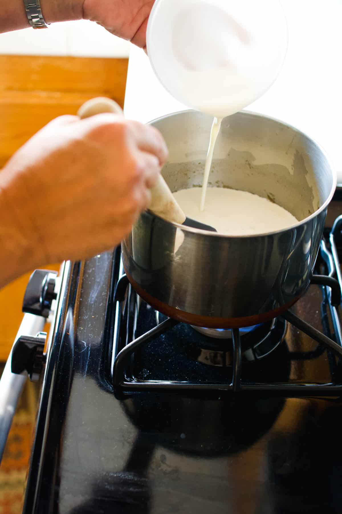 Woman adding cream to a saucepan on the stove.