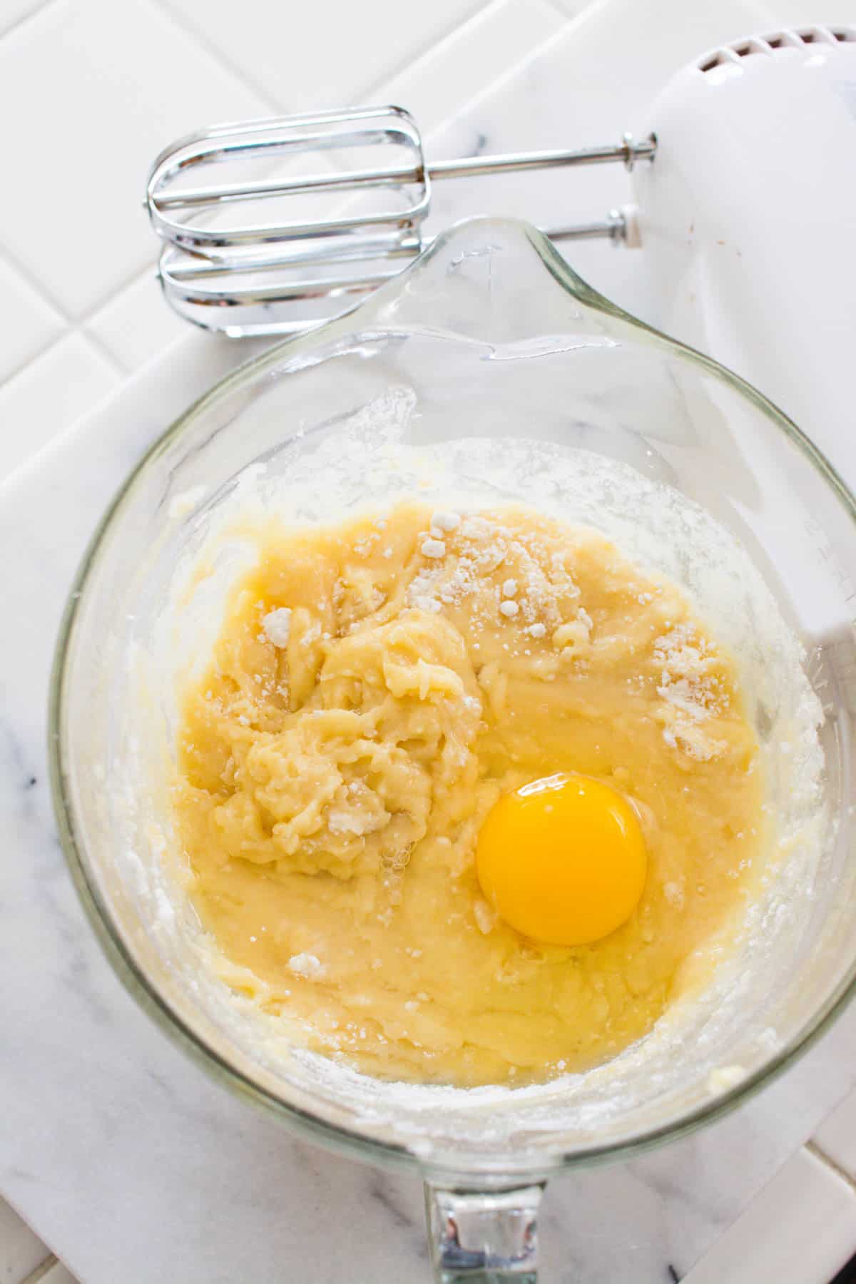 A glass bowl with cake batter and an egg.