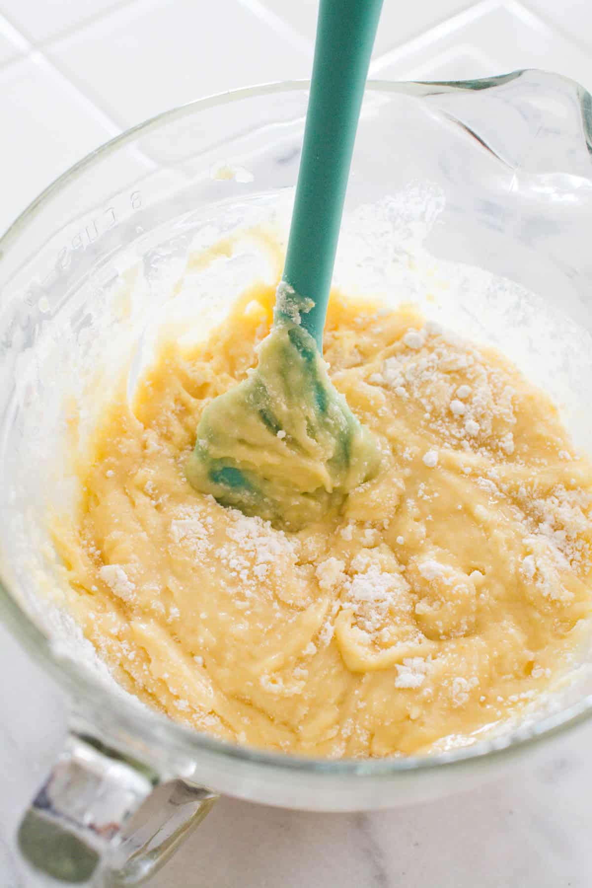 A cake batter being mixed by a spatula in a glass mixing bowl.