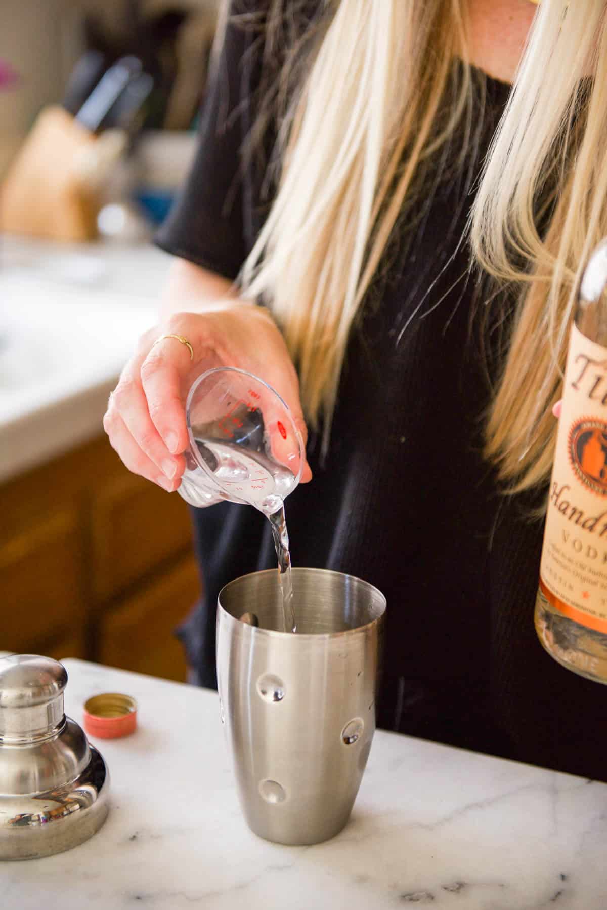 Woman adding vodka to a cocktail shaker.