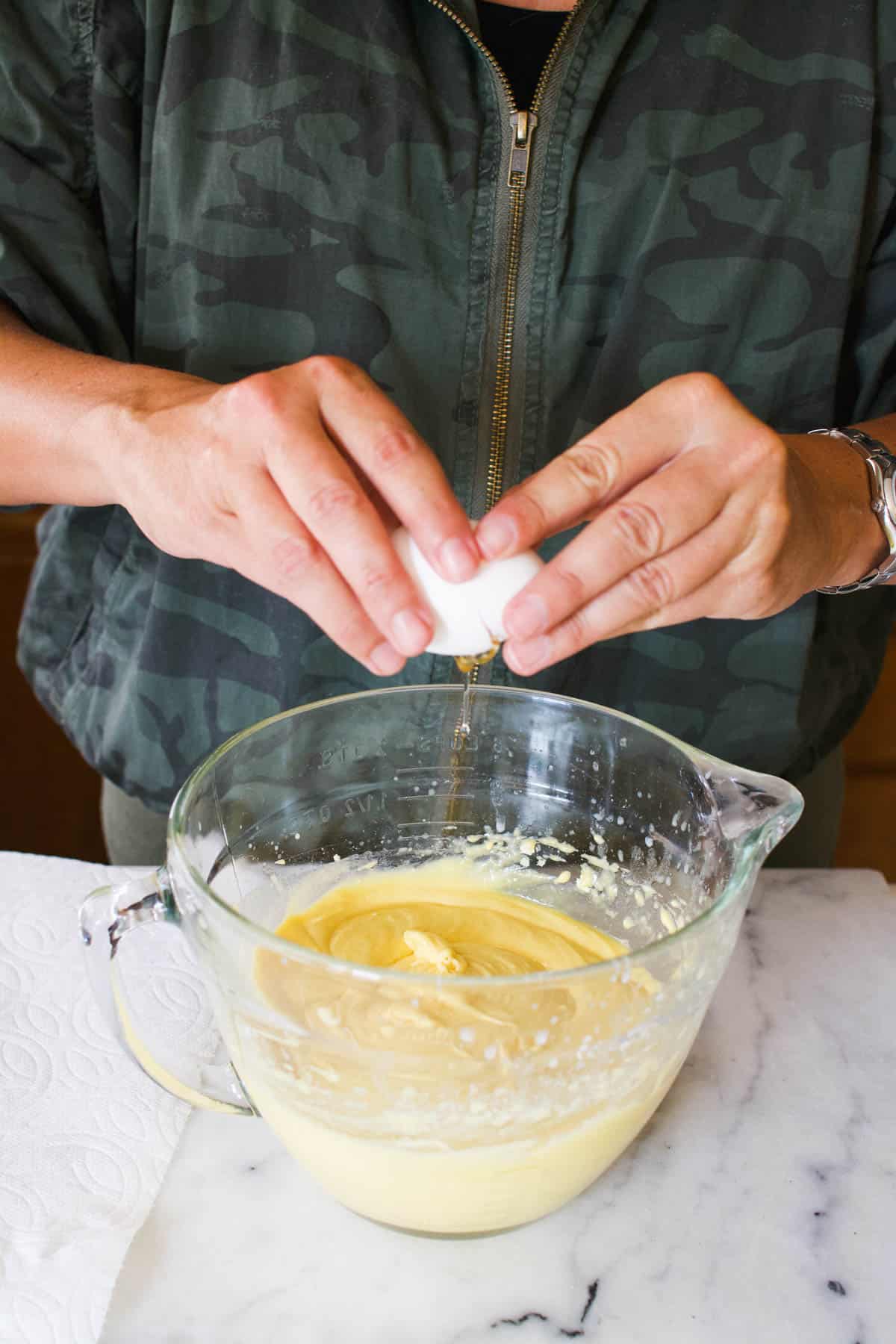 Woman adding eggs to batter bowl with cake batter.