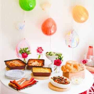 A party table with lasagnas and balloons on the wall.