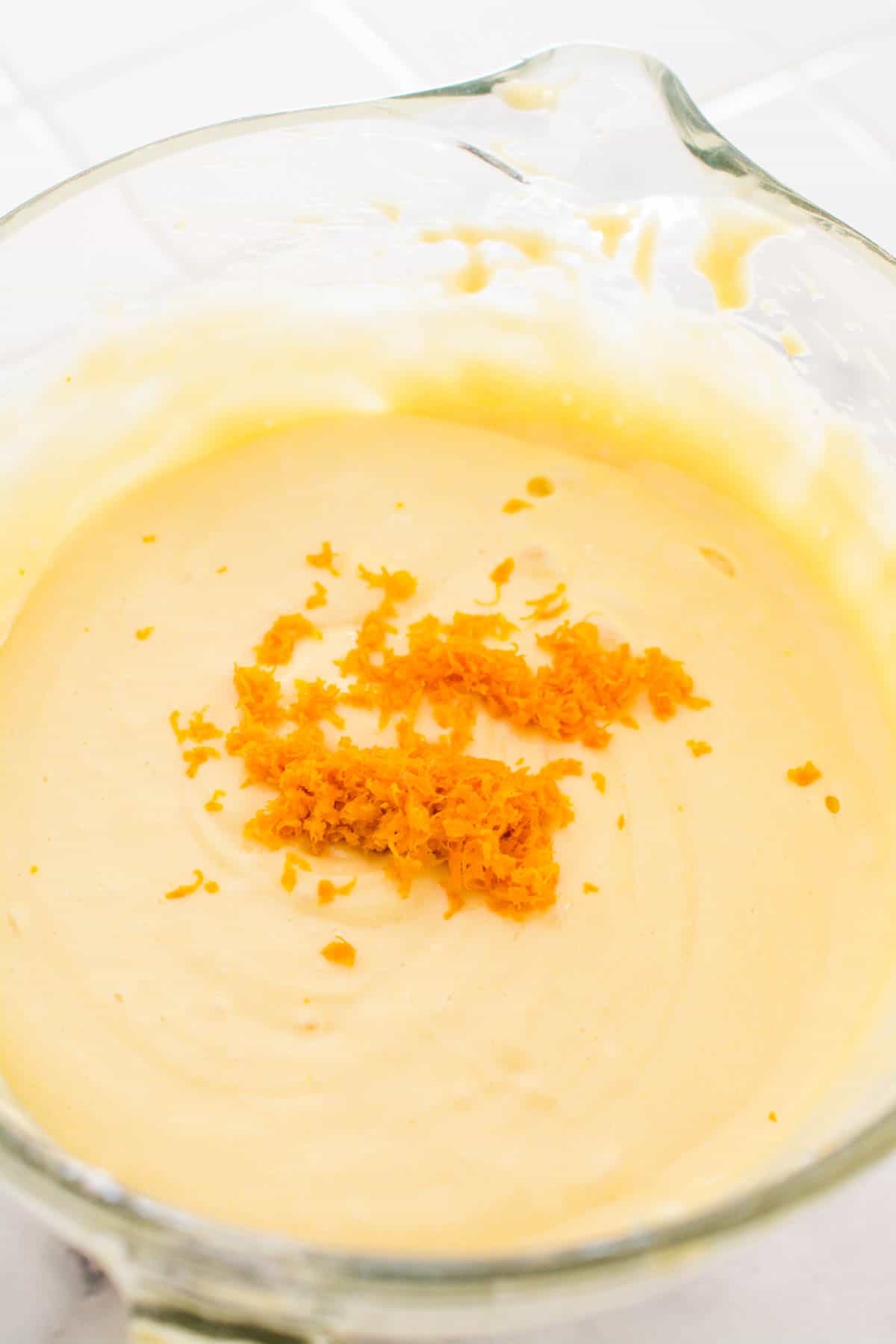 Cake batter in a glass bowl with orange zest on top.