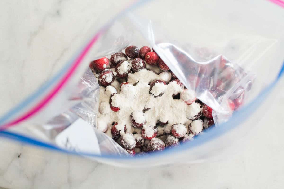 A plastic storage bag with fresh cranberries and some flour.
