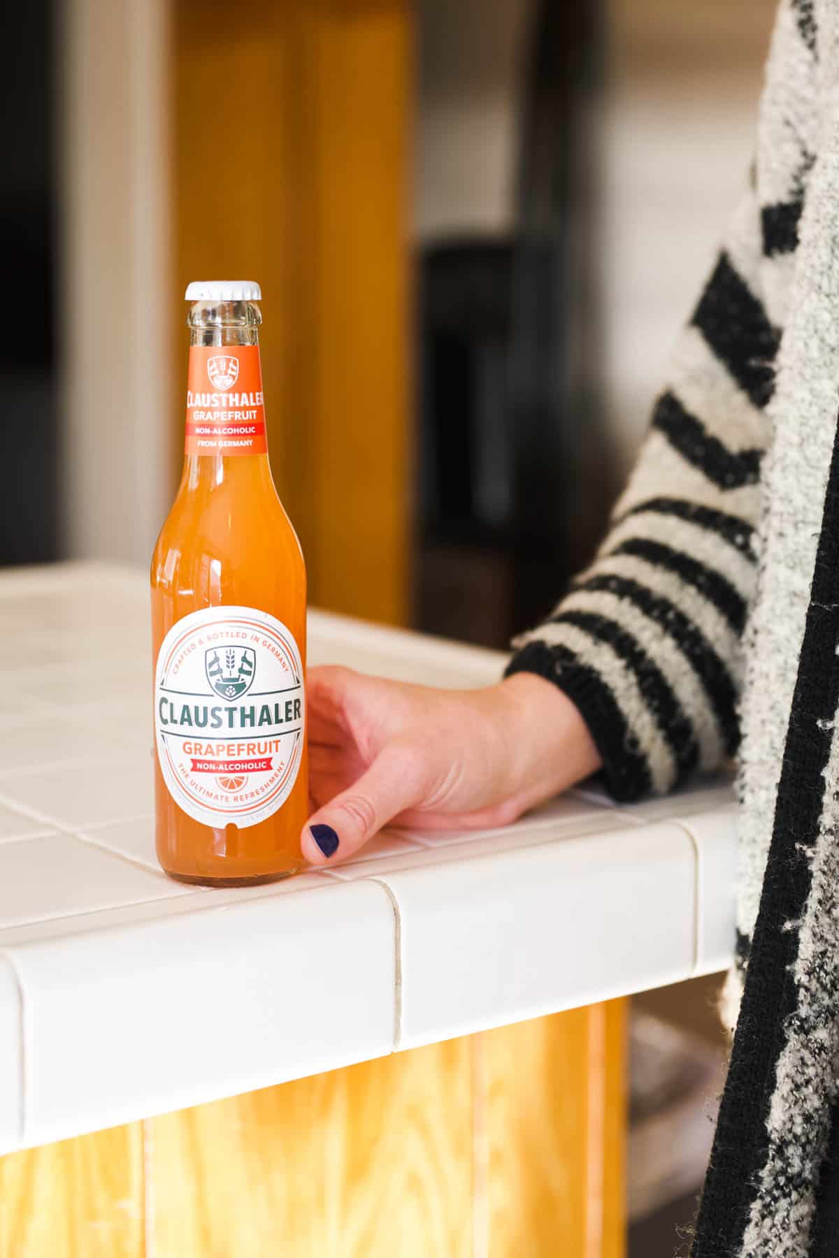 Woman holding on to a bottle of non-alcoholic beer on a counter.