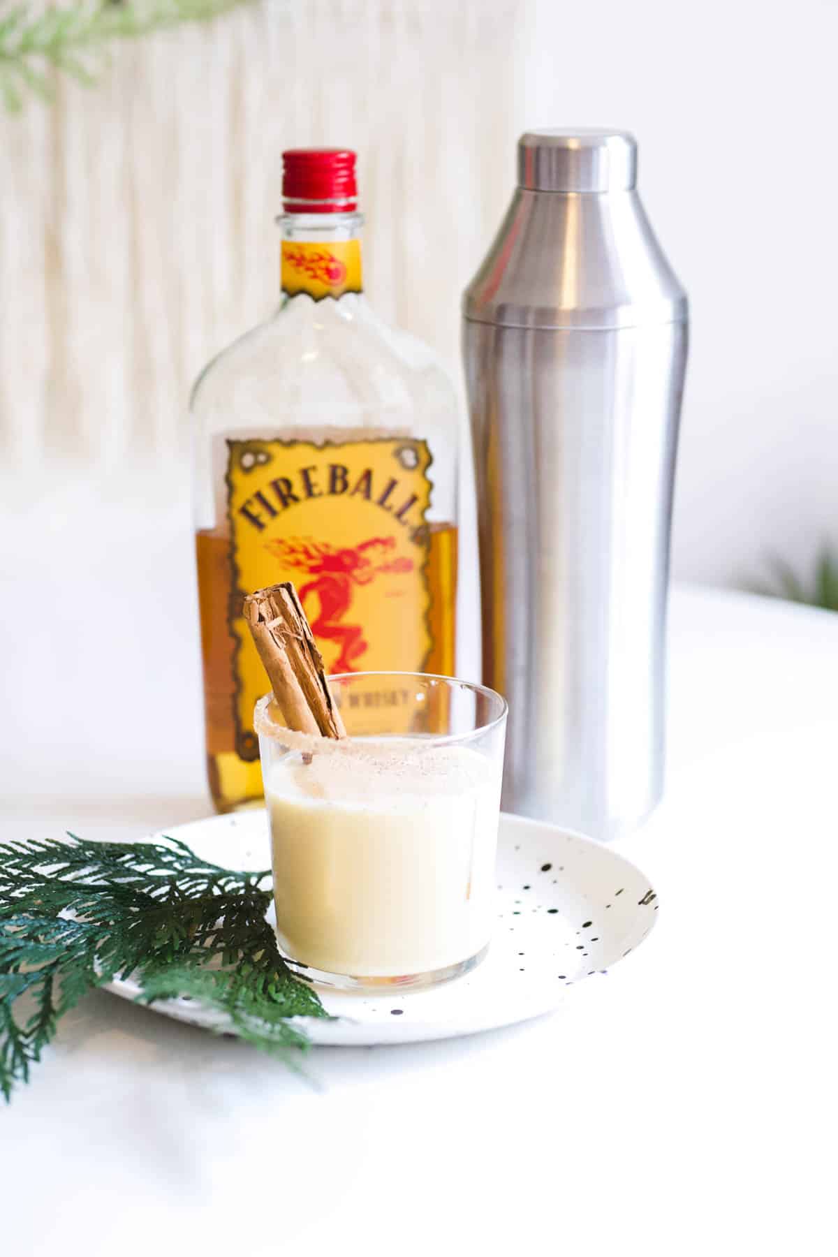 Cocktail with Fireball and Eggnog in a glass next to a cocktail shaker and bottle of Fireball.