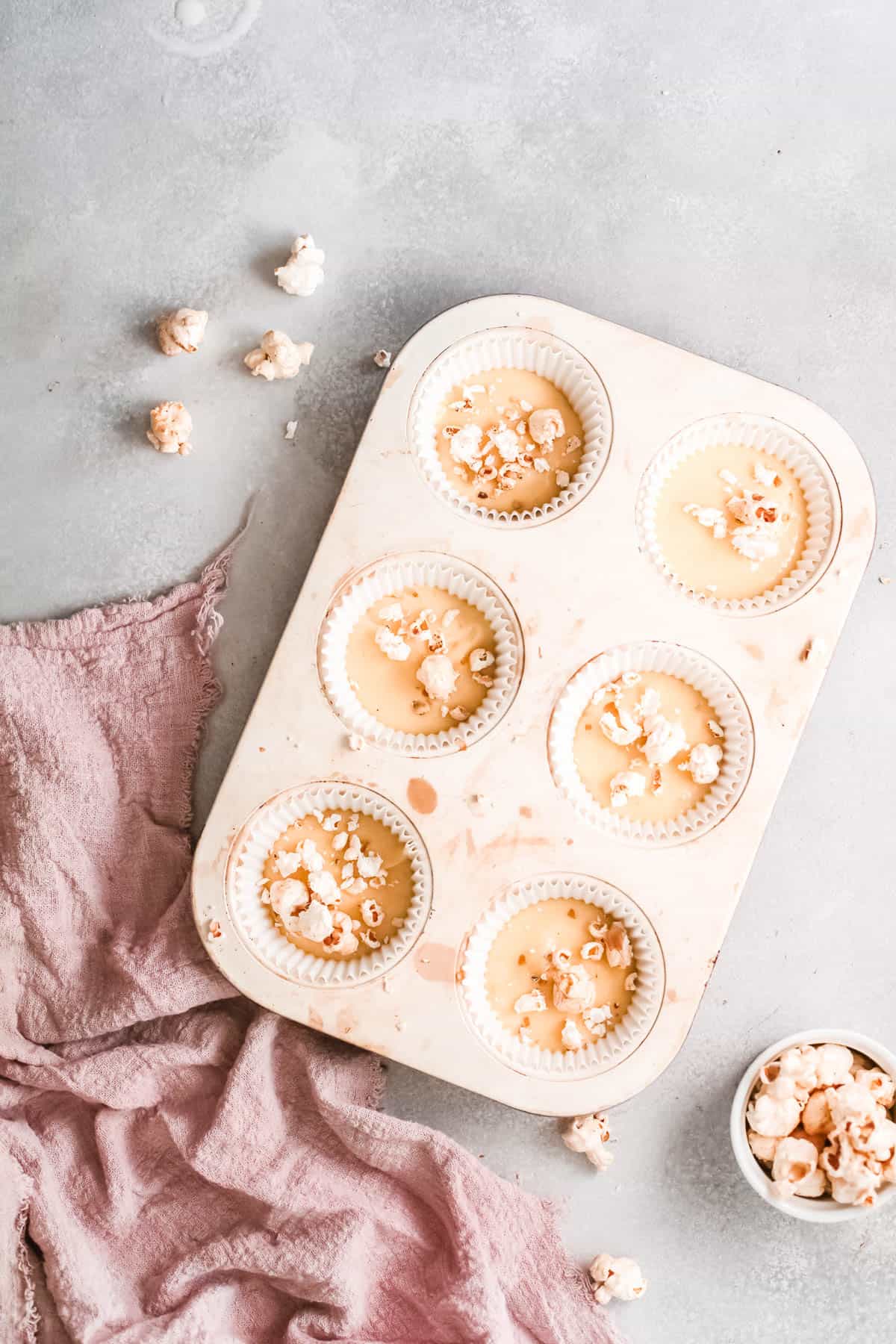 A cupcake tin with cupcake batter and some crushed popcorn on top.