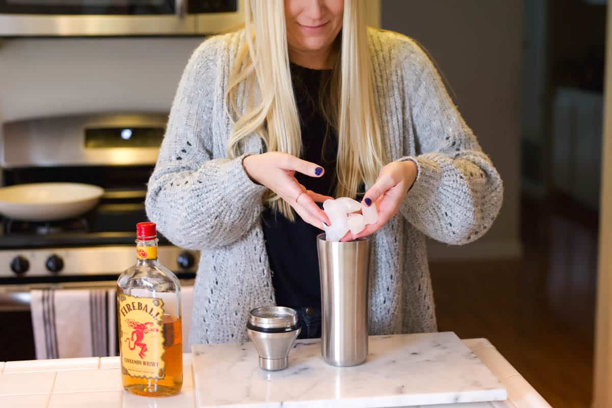 Woman adding ice to a cocktail shaker on a counter.