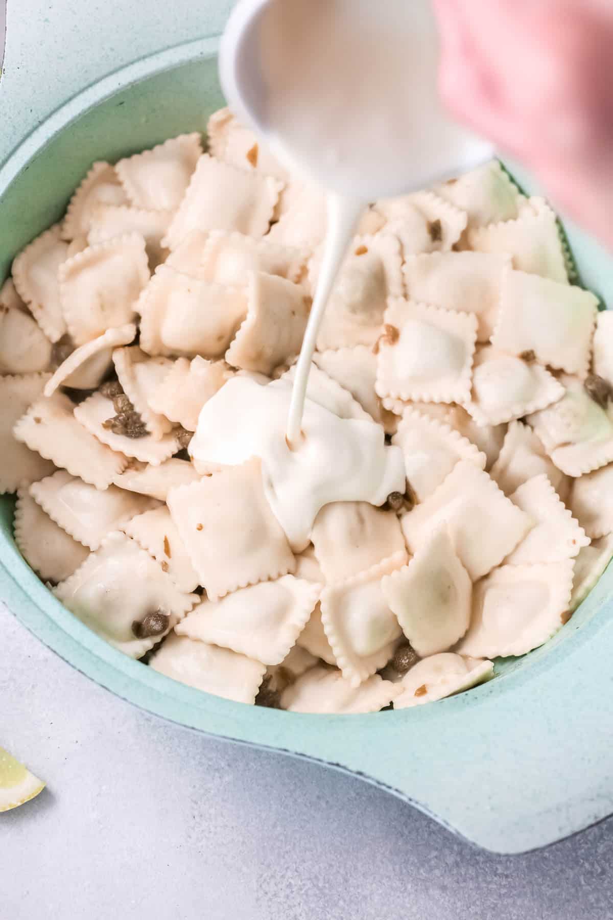 A bowl with ravioli and a woman adding heavy cream.