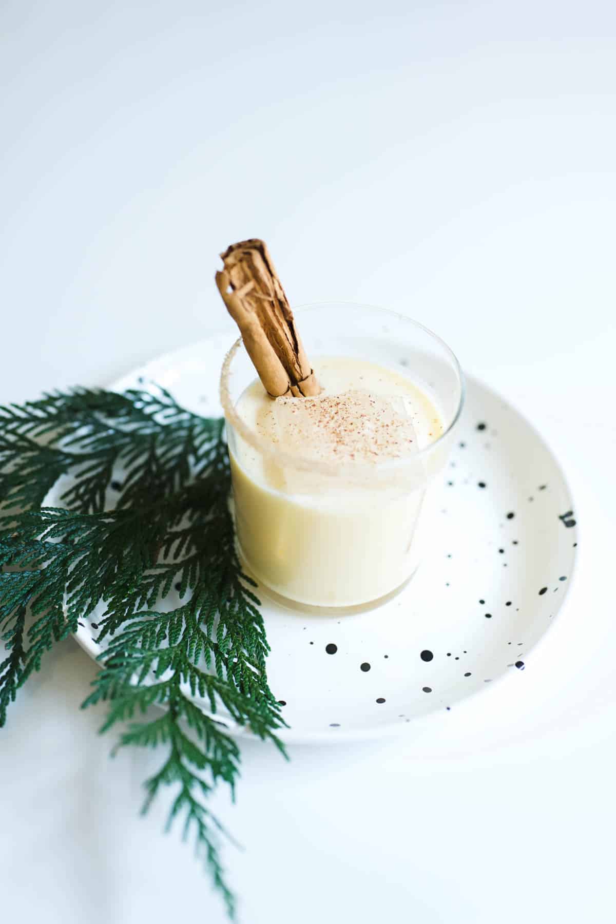 A Fireball Eggnog cocktail in a cup on a table with a cinnamon stick garnish.