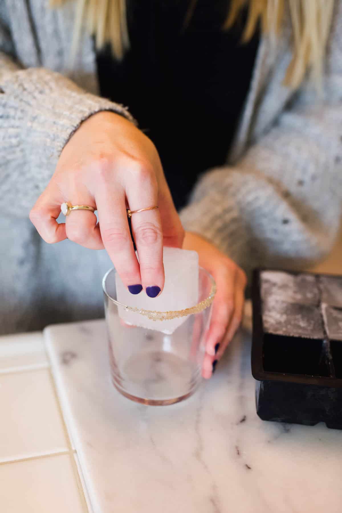 Woman adding a large square ice cube to a cocktail glass.