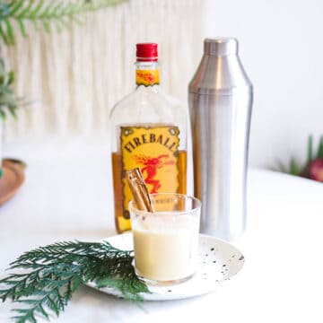 A Fireball Eggnog cocktail on a table next to a cocktail shaker and Fireball bottle.