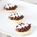 Square image of decorated football sugar cookies on a white plate.