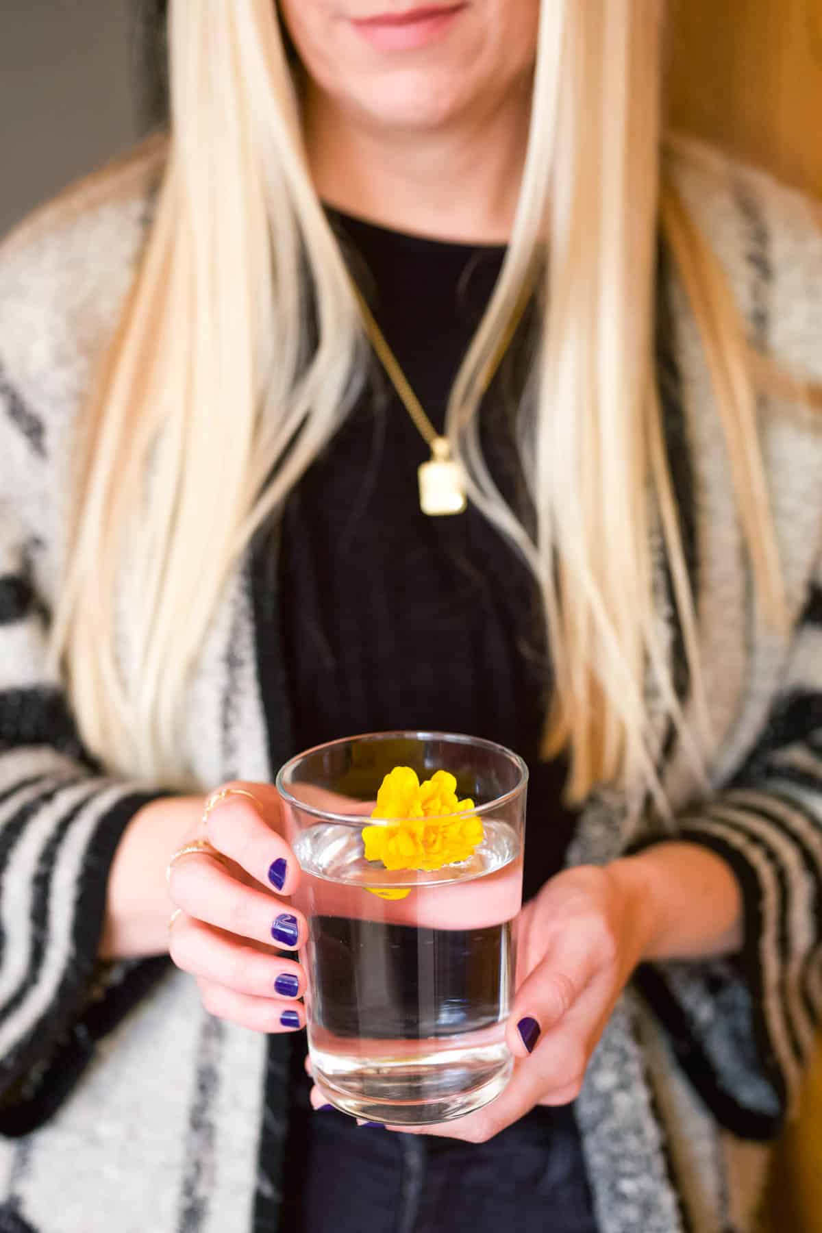 Blonde woman holding a glass of water with a flower in it.