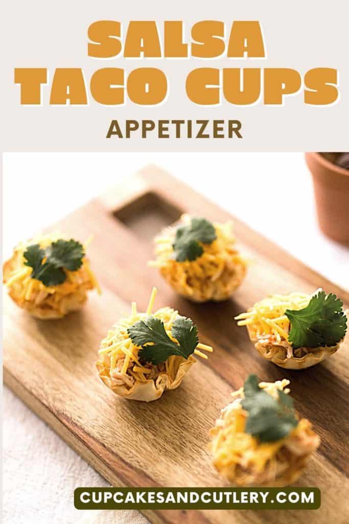 Close up of chicken taco cups with shredded cheese and cilantro on a wooden serving board.