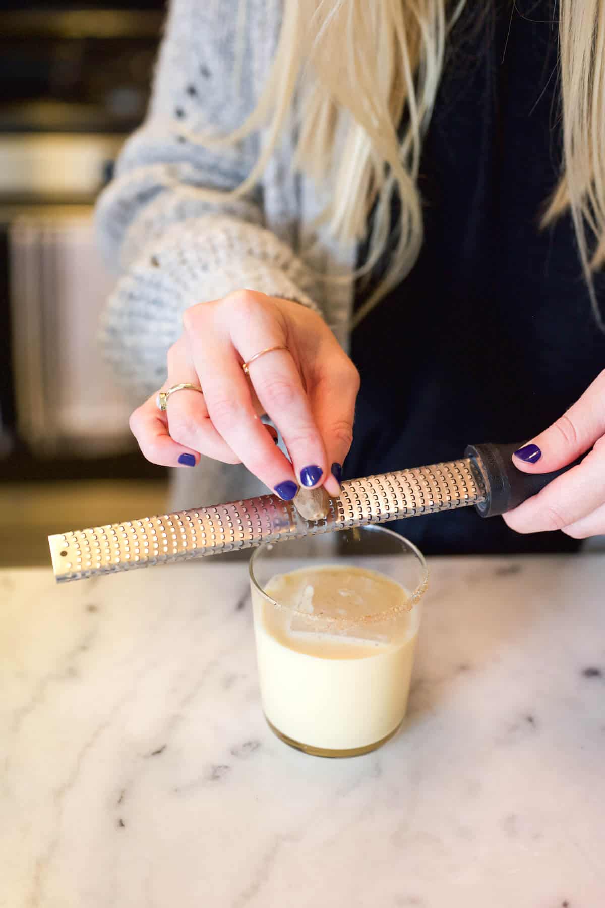 A woman grating fresh nutmeg on top of a Fireball and Eggnog cocktail.