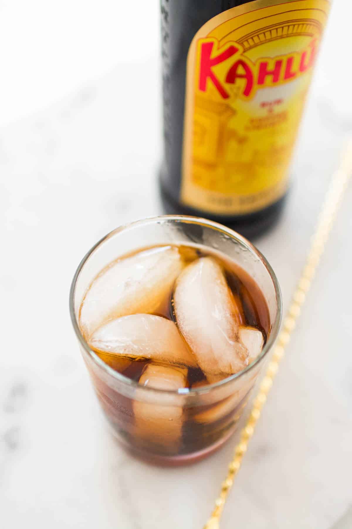 A 2 ingredient Black Russian drink in a glass next to a bottle of Kahlua.
