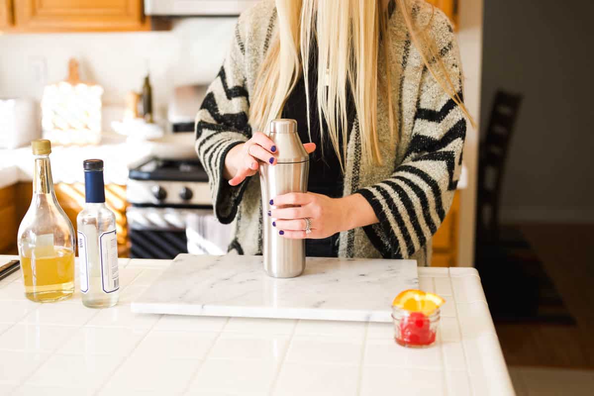 Woman putting the top on a cocktail shaker to make a drink. 