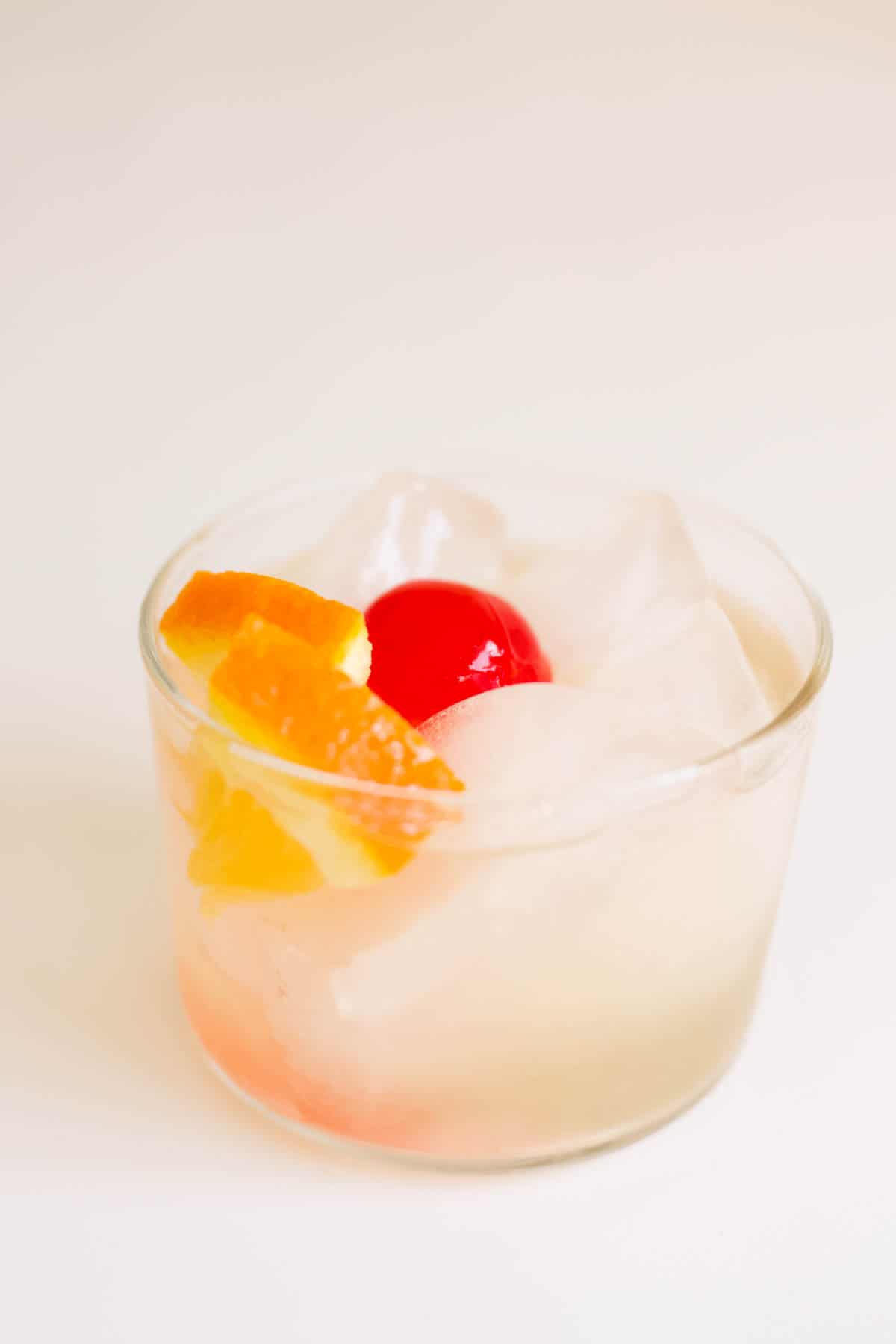 A short cocktail glass with an Amaretto sour garnished with an orange slice and cherry.