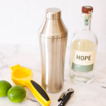 A cocktail shaker and citrus squeezer on a table next to a bottle of vodka.