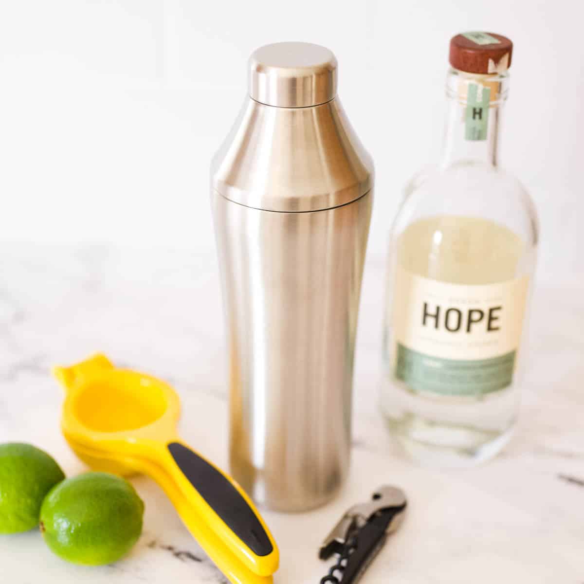 A cocktail shaker and citrus squeezer on a table next to a bottle of vodka.