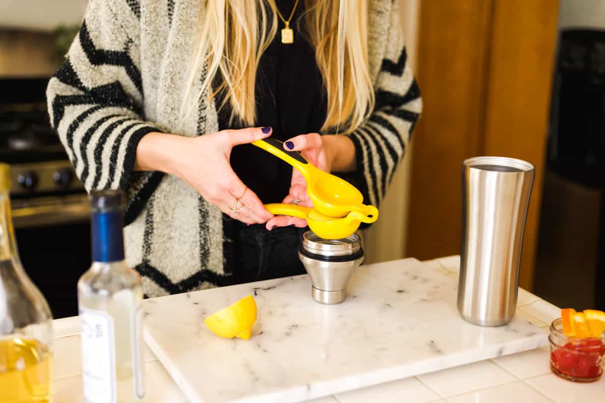 Woman squeezing lemon juice into a cocktail shaker.