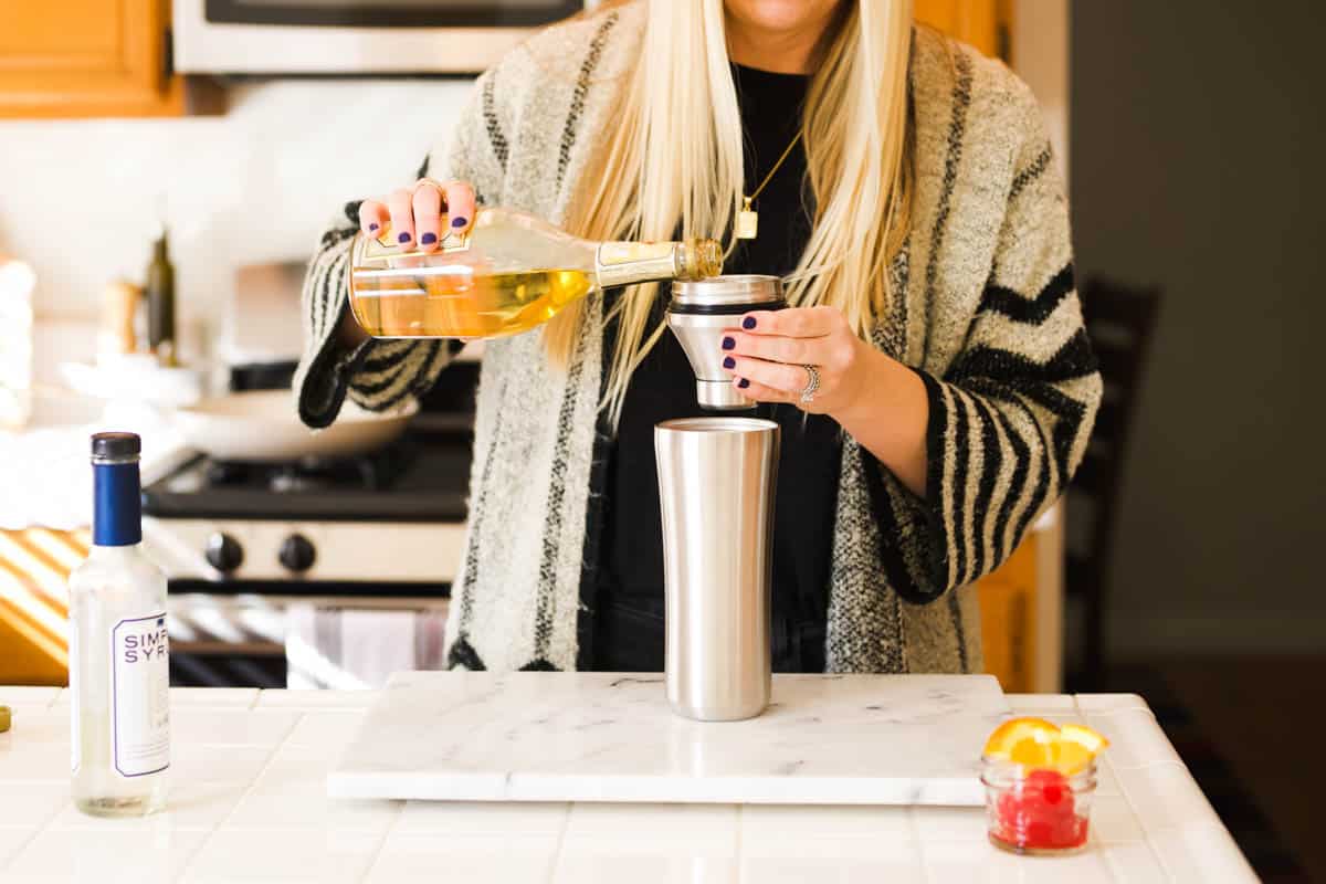 Woman measuring some amaretto in the top of a cocktail shaker.