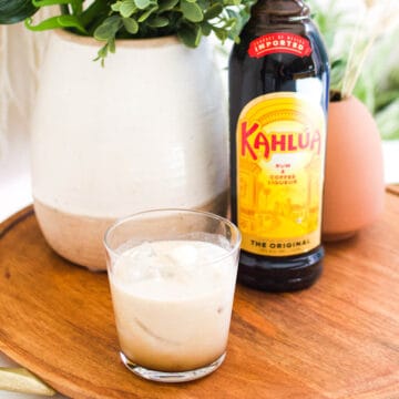 A bottle of Kahlua on a tray with a short cocktail glass with a White Russian cocktail in it.