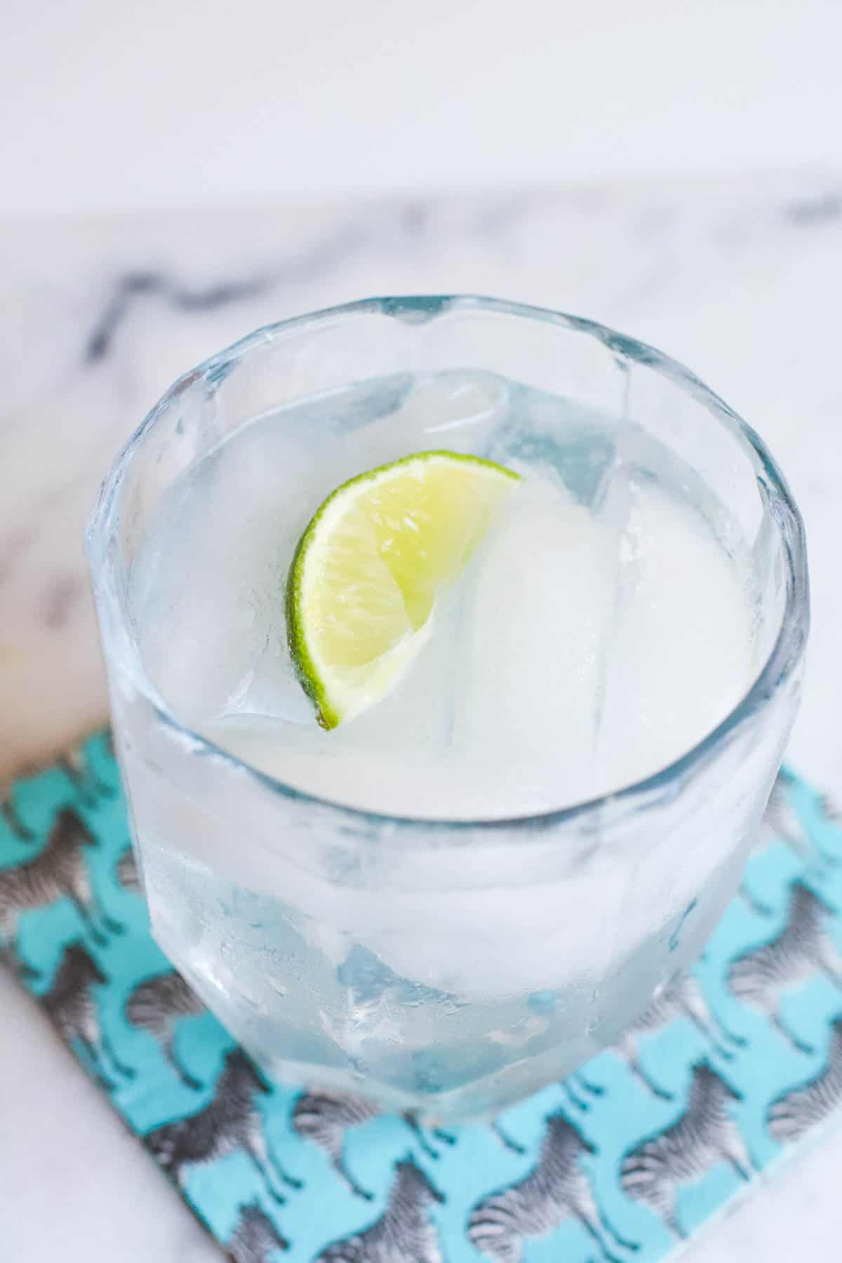 A short glass with ice and a clear cocktail with a lime wedge garnish on a napkin with zebras on it.