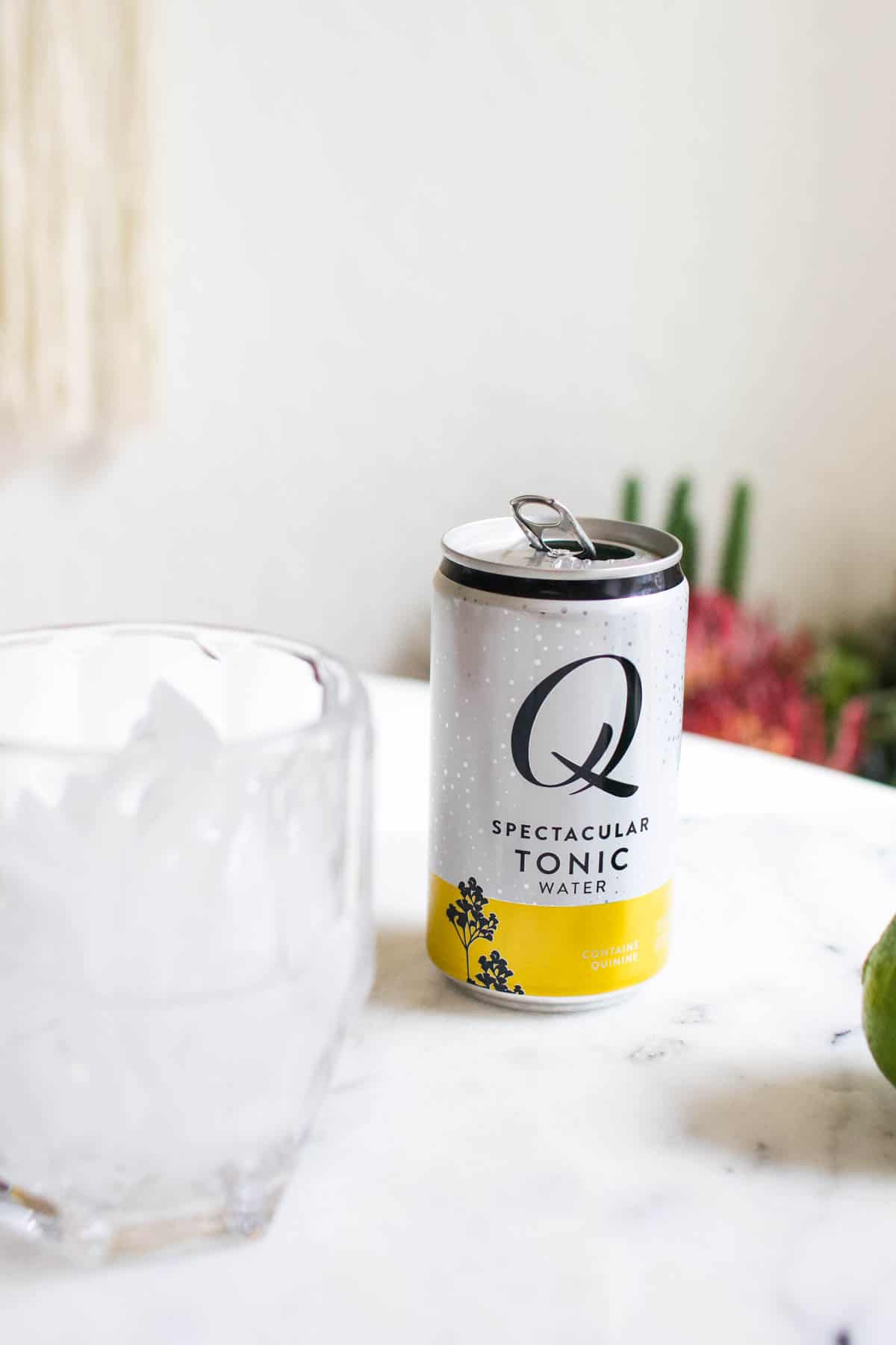 A can of tonic on a table next to a glass with ice in it. 