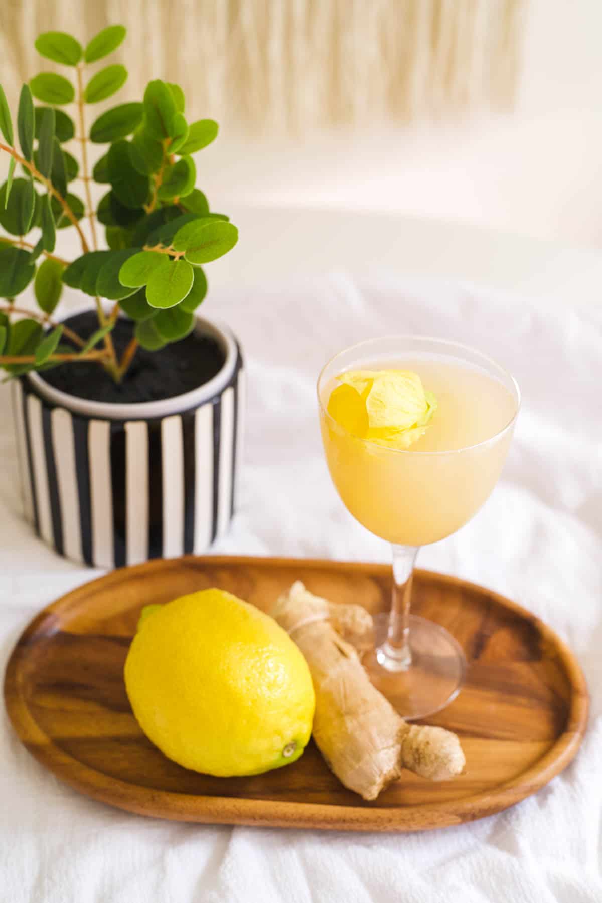 A lemon tequila cocktail in a Nick and Nora cocktail glass on a small wooden tray on a table.