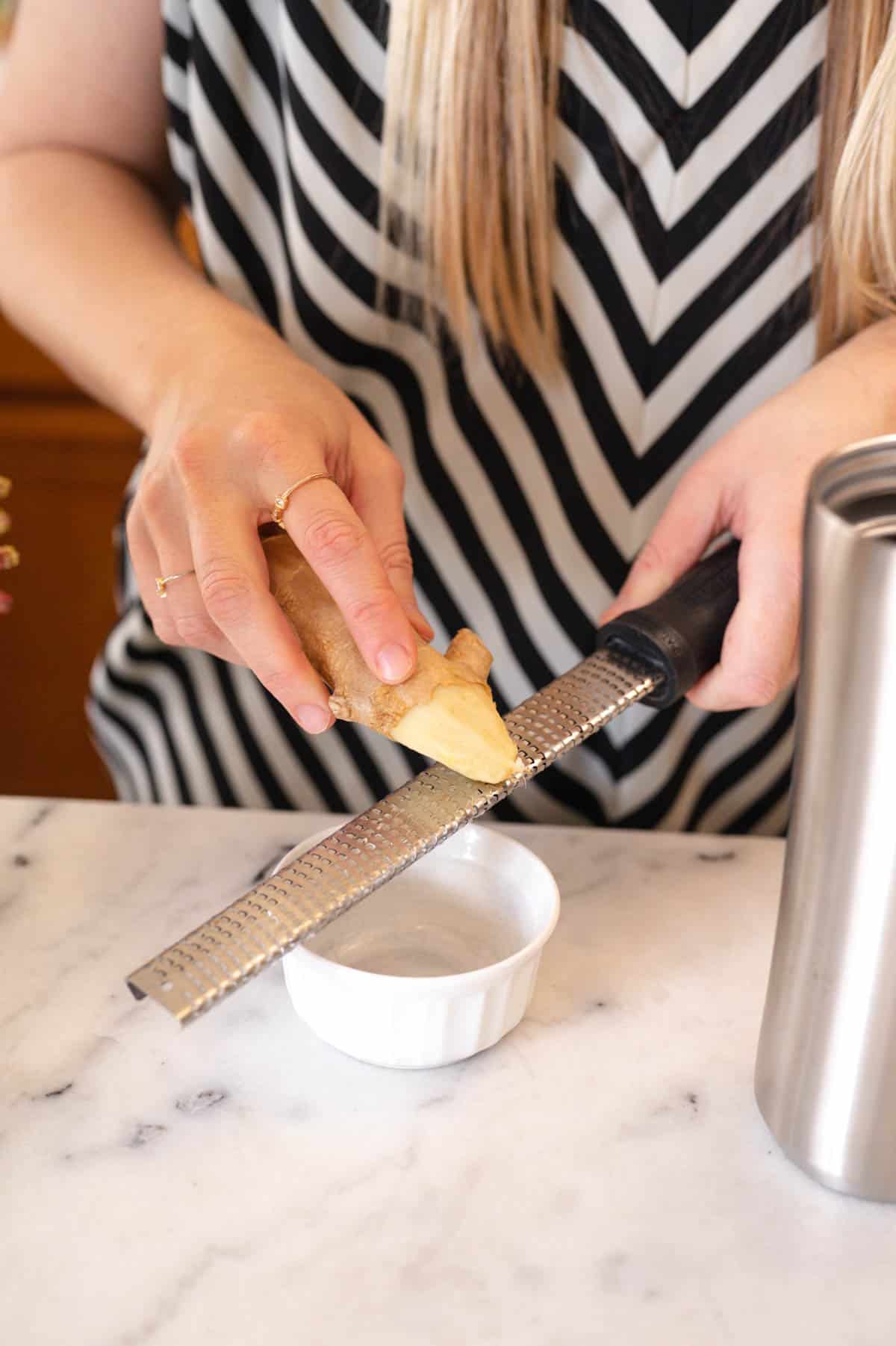 Woman grating fresh ginger on a microplane.