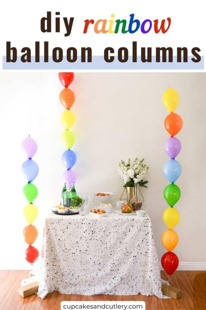 Text - DIY Rainbow Balloon Columns with a party table flanked by 3 homemade balloon columns made with rainbow colored balloons.