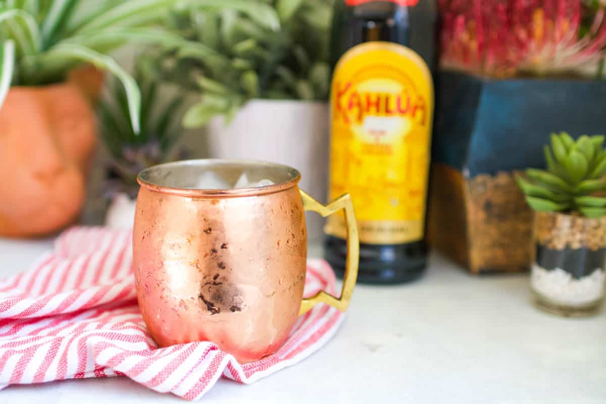 A copper mug in front of a bottle of Kahlua on a table.