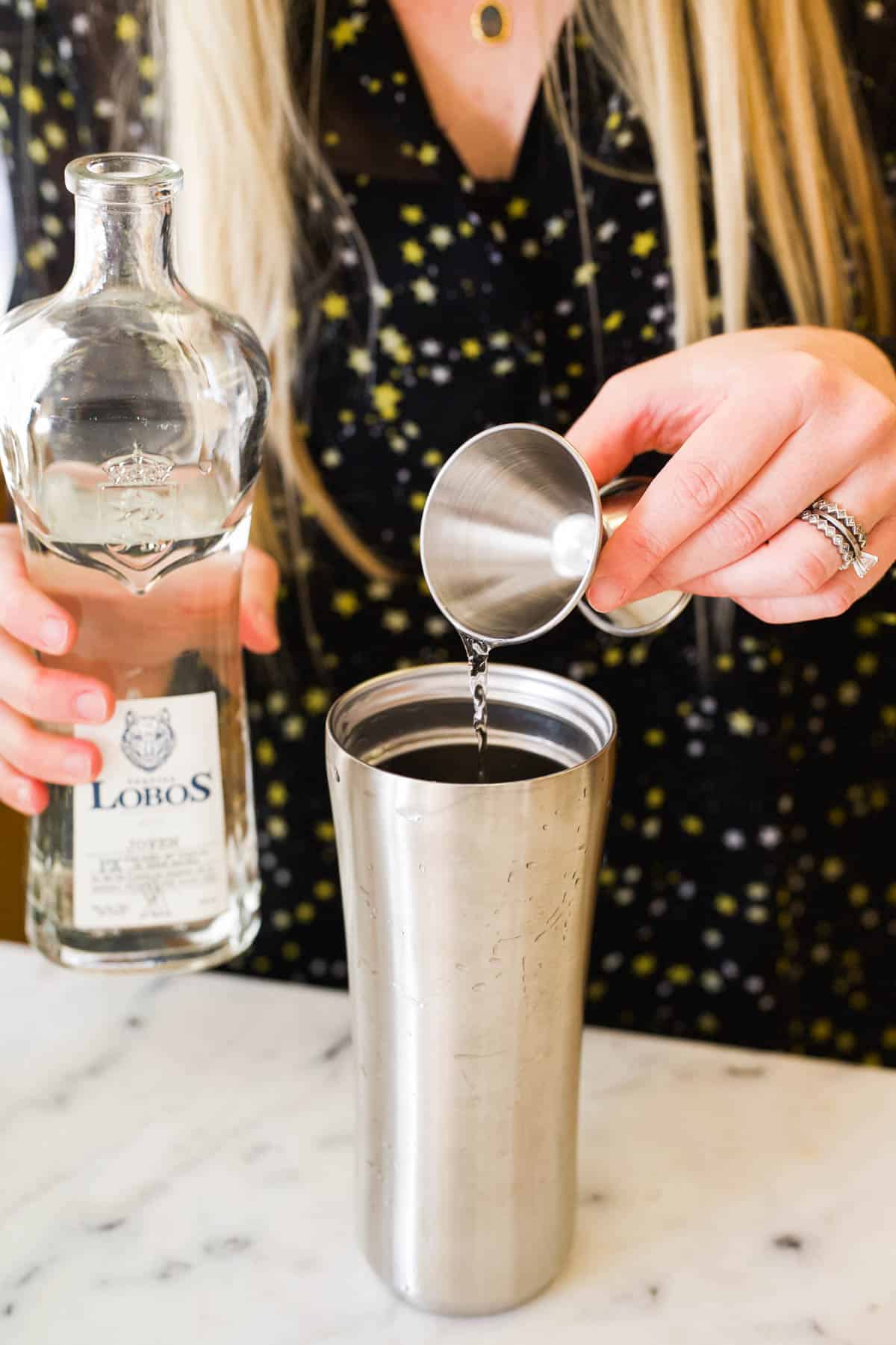 Woman pouring tequila from a jigger into a cocktail shaker.