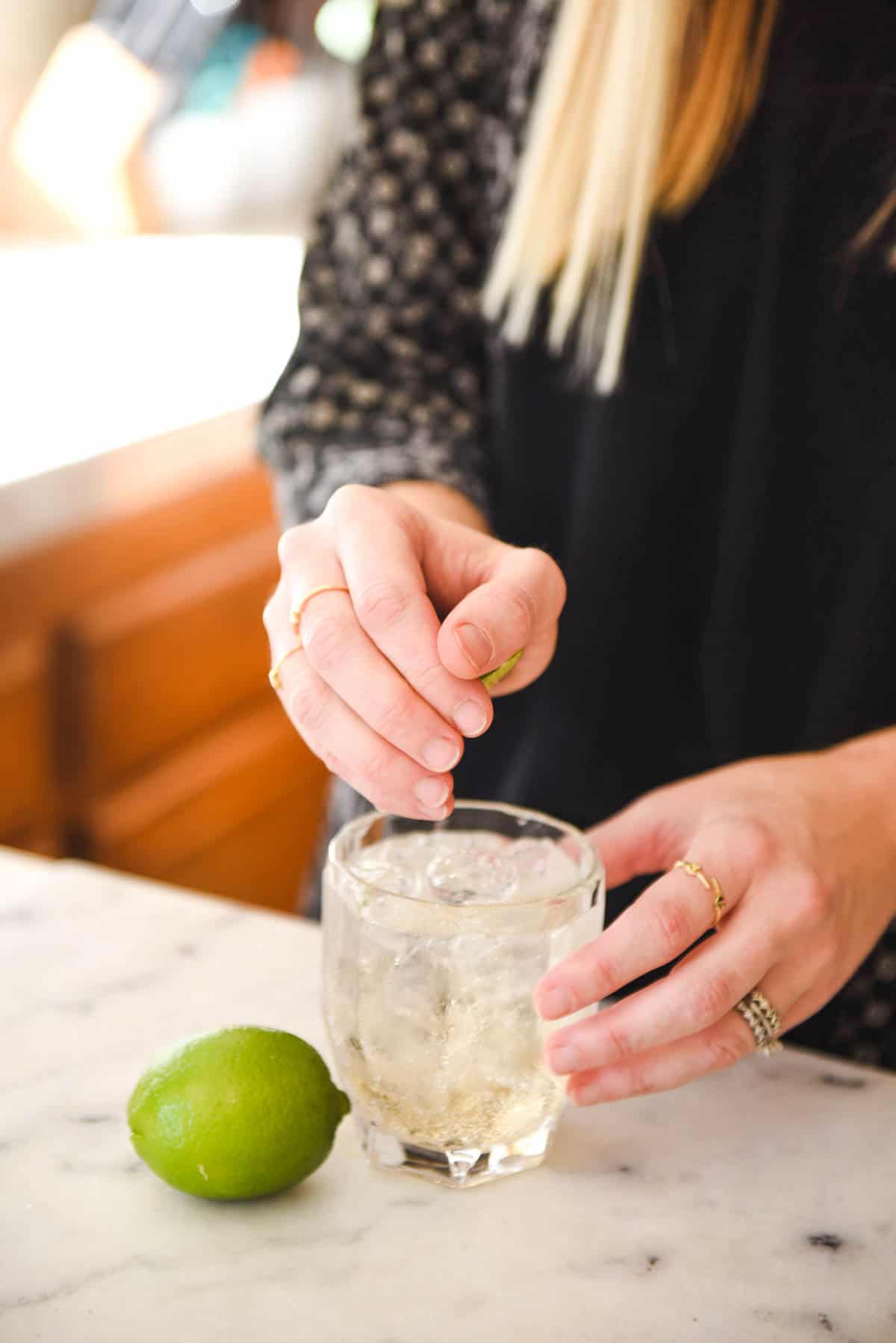 A woman squeezing a lime into a cocktail.