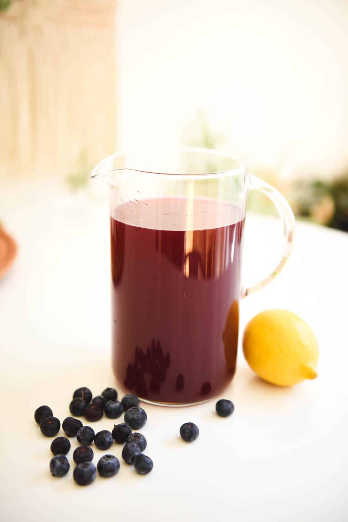 A lemonade flavored with blueberry in a pitcher on a table.