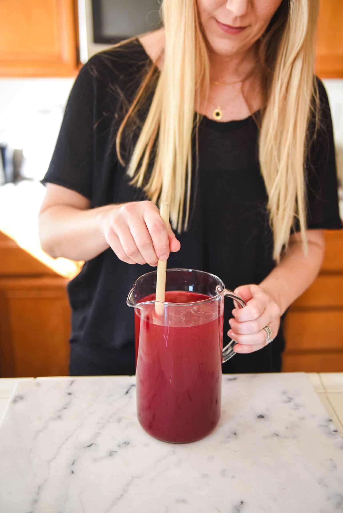 Woman stirring blueberry lemonade in a pitcher.