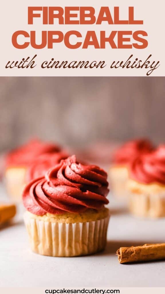 Text: Fireball Cupcakes with Cinnamon Whisky with a red frosted cupcake on a table with more in the background.
