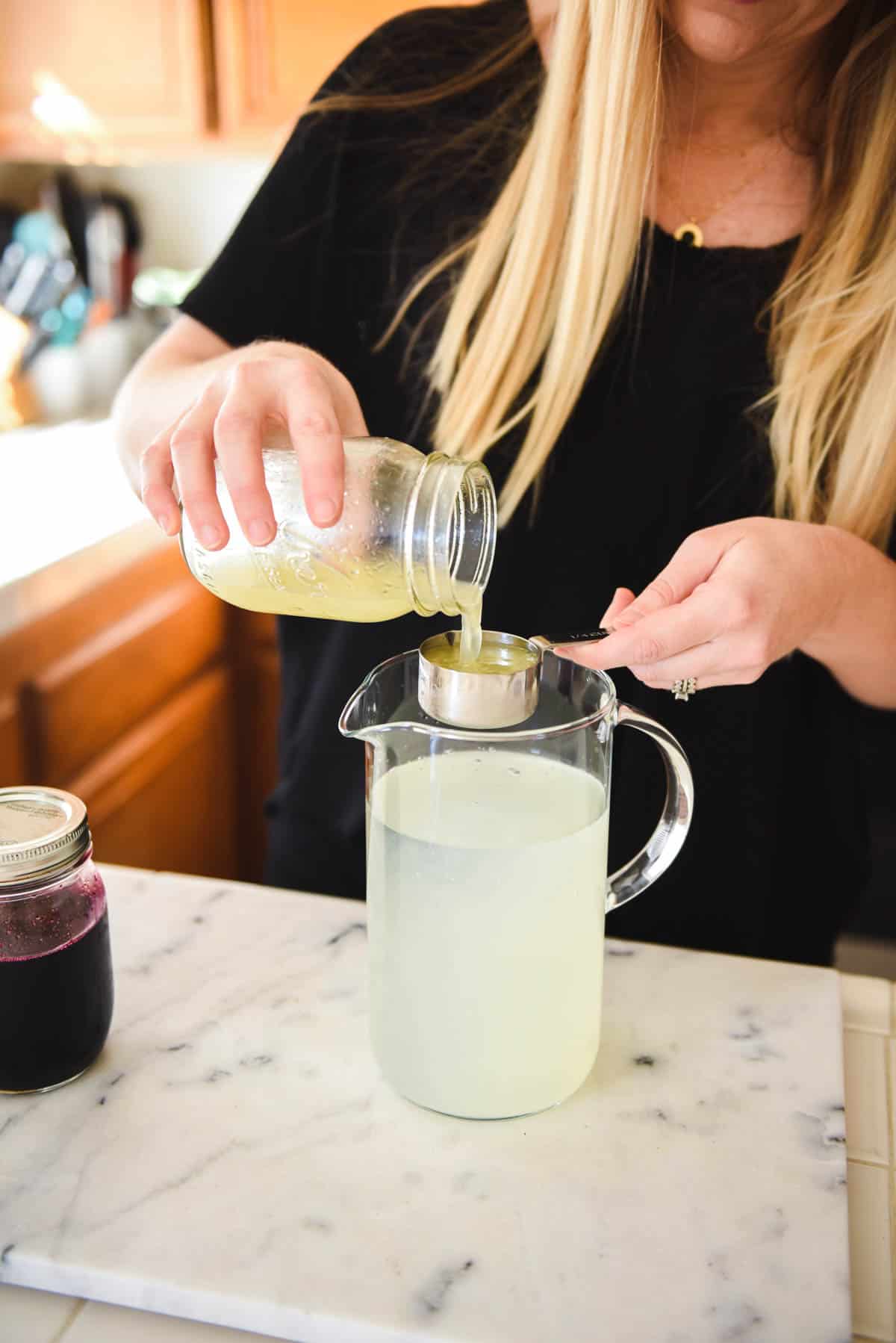 Woman measuring fresh lemon juice into a pitcher of water.