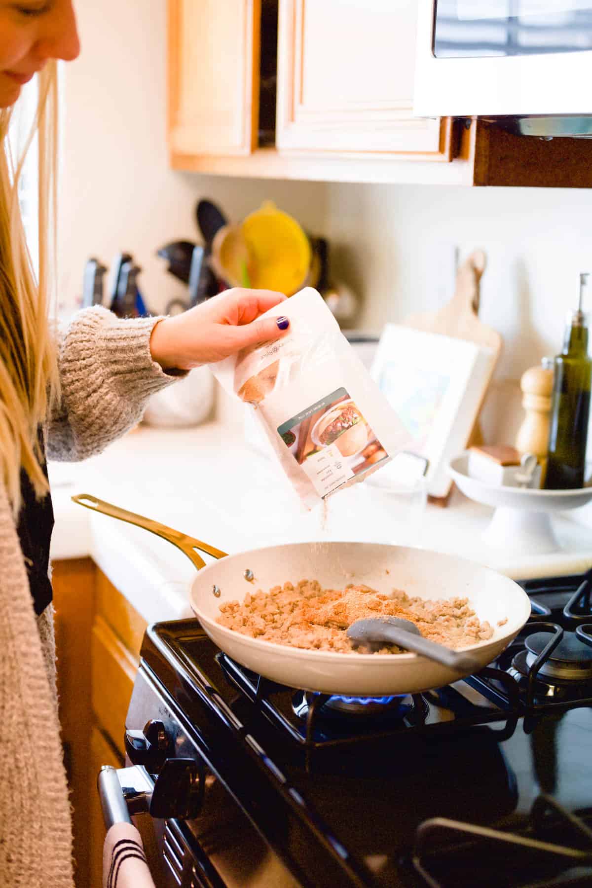 Woman adding a Spice 'n Easy recipe mix to a pan on the stove.