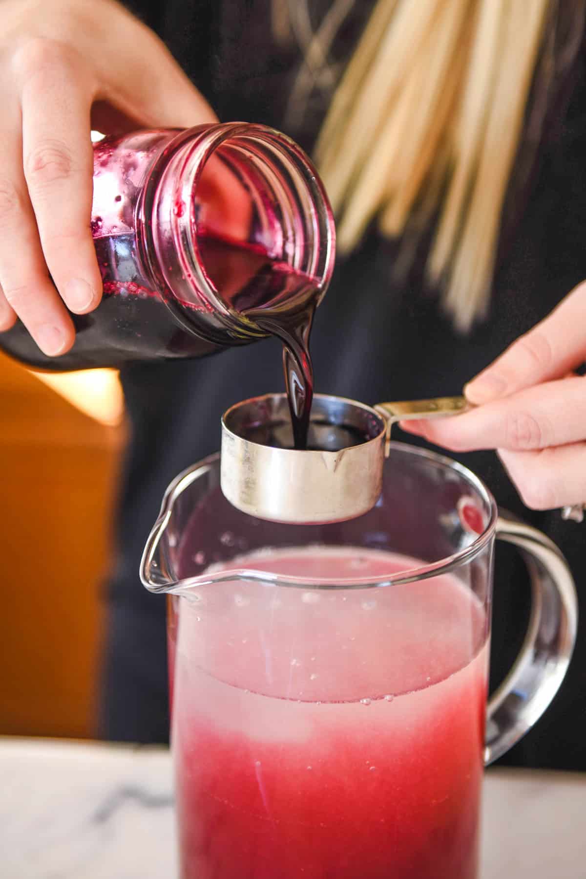 Woman measuring blueberry simple syrup to add to a pitcher.