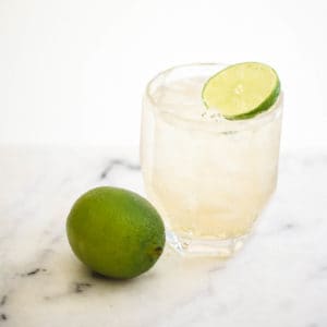 A Tequila and Ginger Ale in a short cocktail glass with a lime wedge and lime next to it.