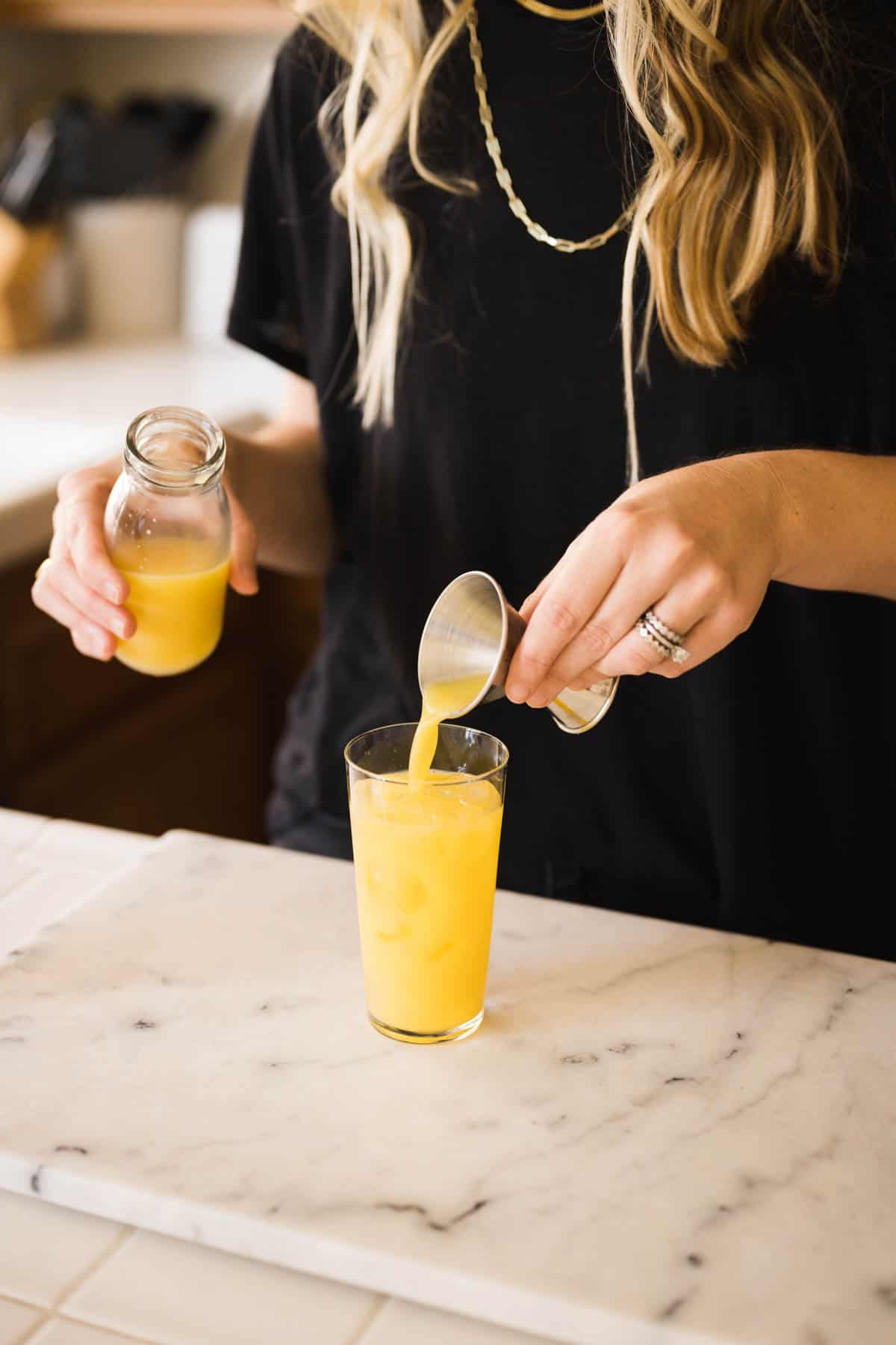 Woman adding orange juice to a cocktail glass from a jigger.