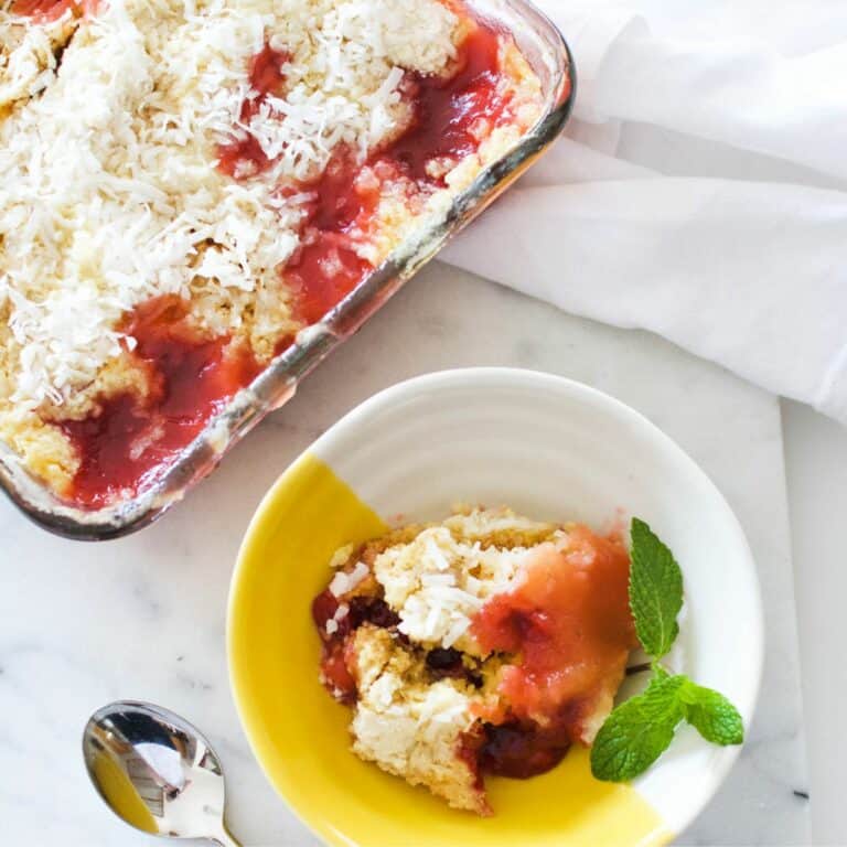 A baking dish with a microwave dump cake with a bowl and a single serving of cherry dump cake.