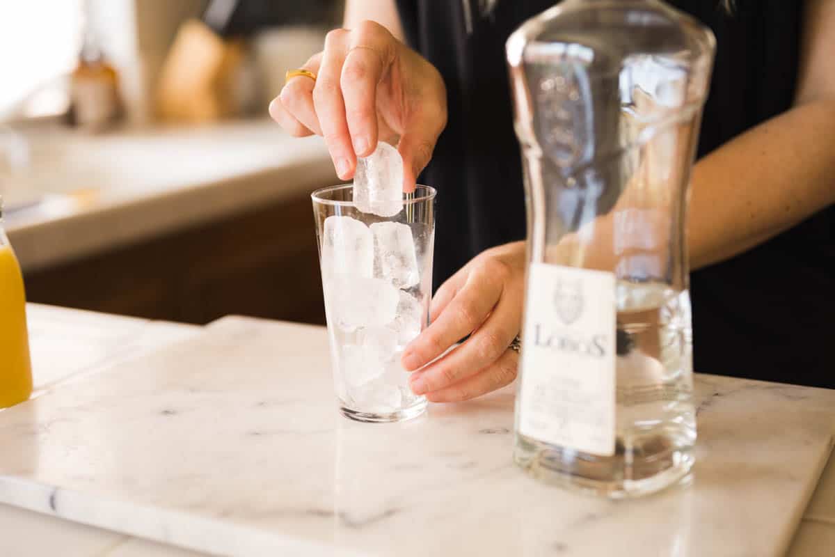 Woman adding ice to a glass with a bottle of tequila on the counter next to her.
