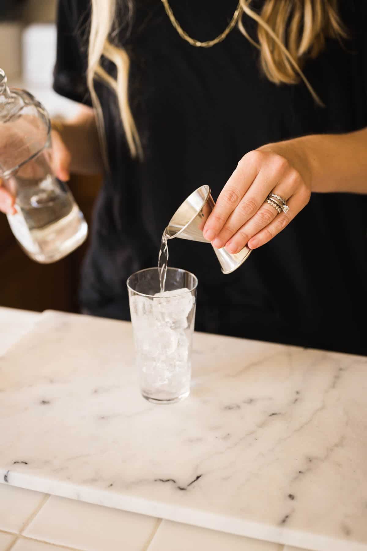 Woman adding tequila to a cocktail glass.