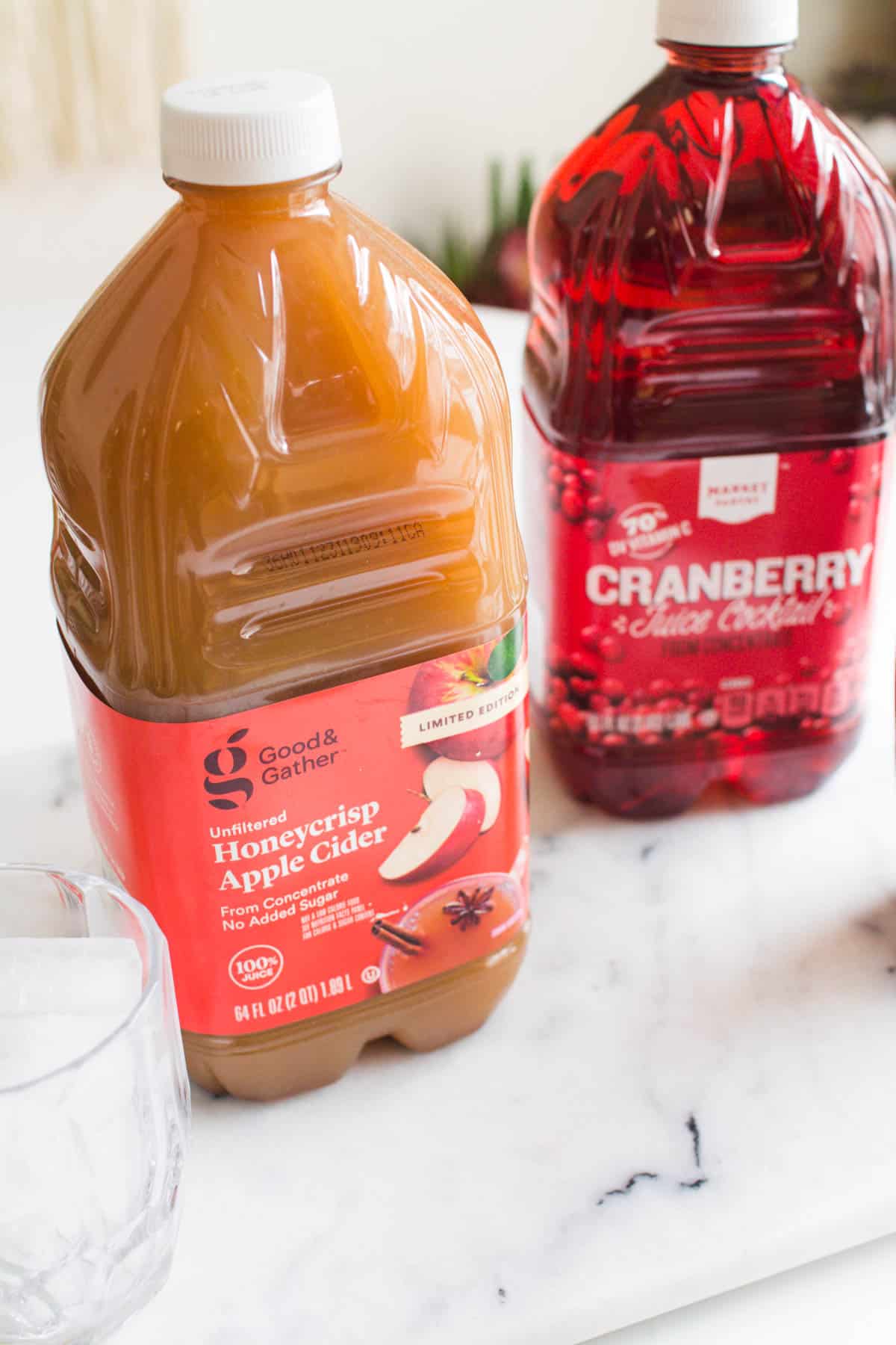 2 large bottles of juice on a table next to a glass of ice.