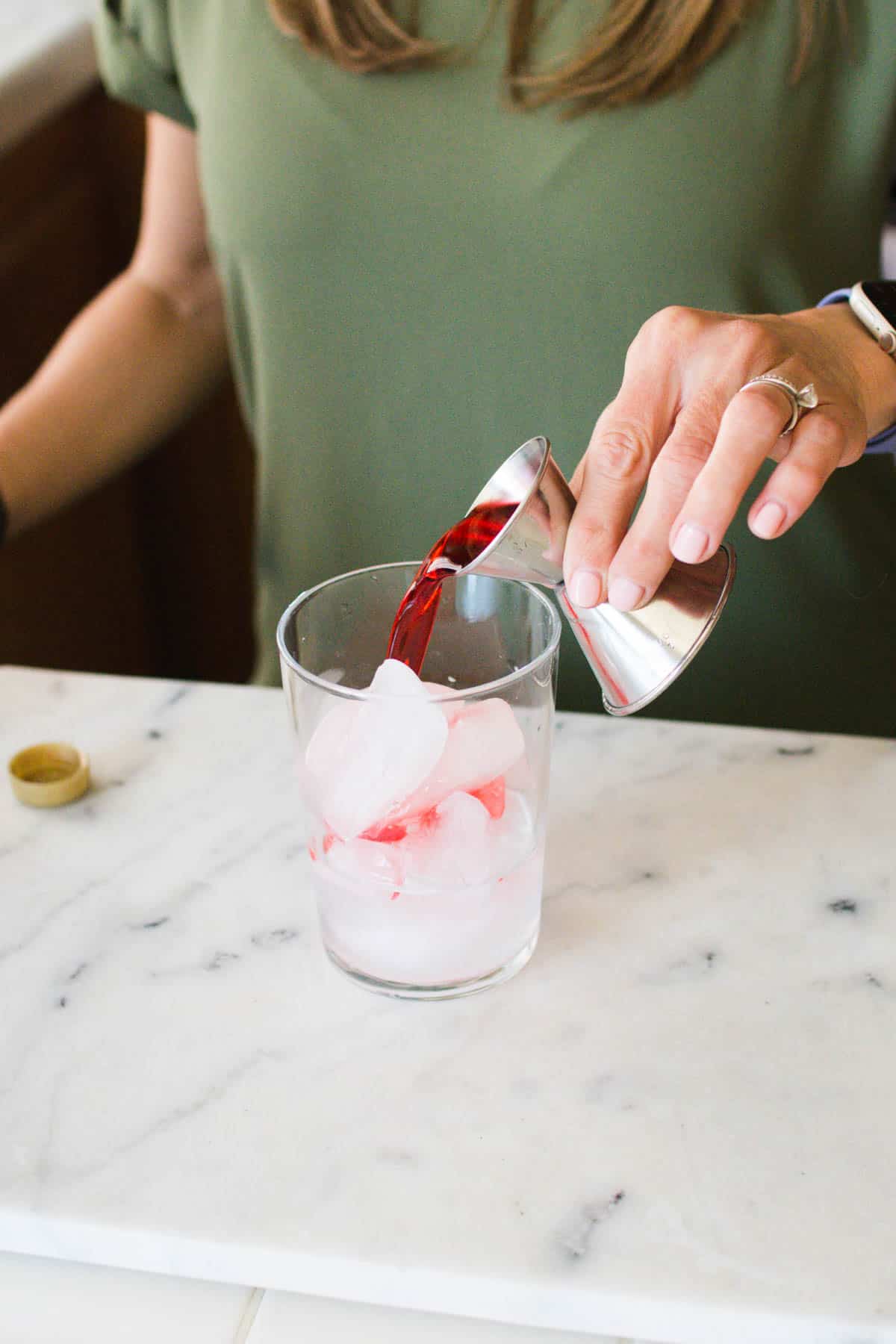 Woman adding grenadine to a cup of ice.