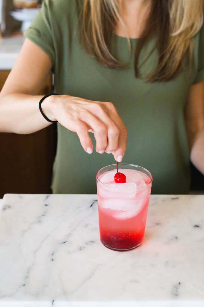Woman adding a cherry to the top of a cocktail.